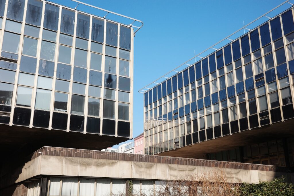 Ein Foto der Prager Würfel, einem ikonischen brutalistischen Gebäudekomplex in Prag, aufgenommen aus verschiedenen Blickwinkeln. Die Bilder zeigen die charakteristischen Betonstrukturen und die einzigartige Architektur der Gebäude, die sich in einem grünen Park befinden.